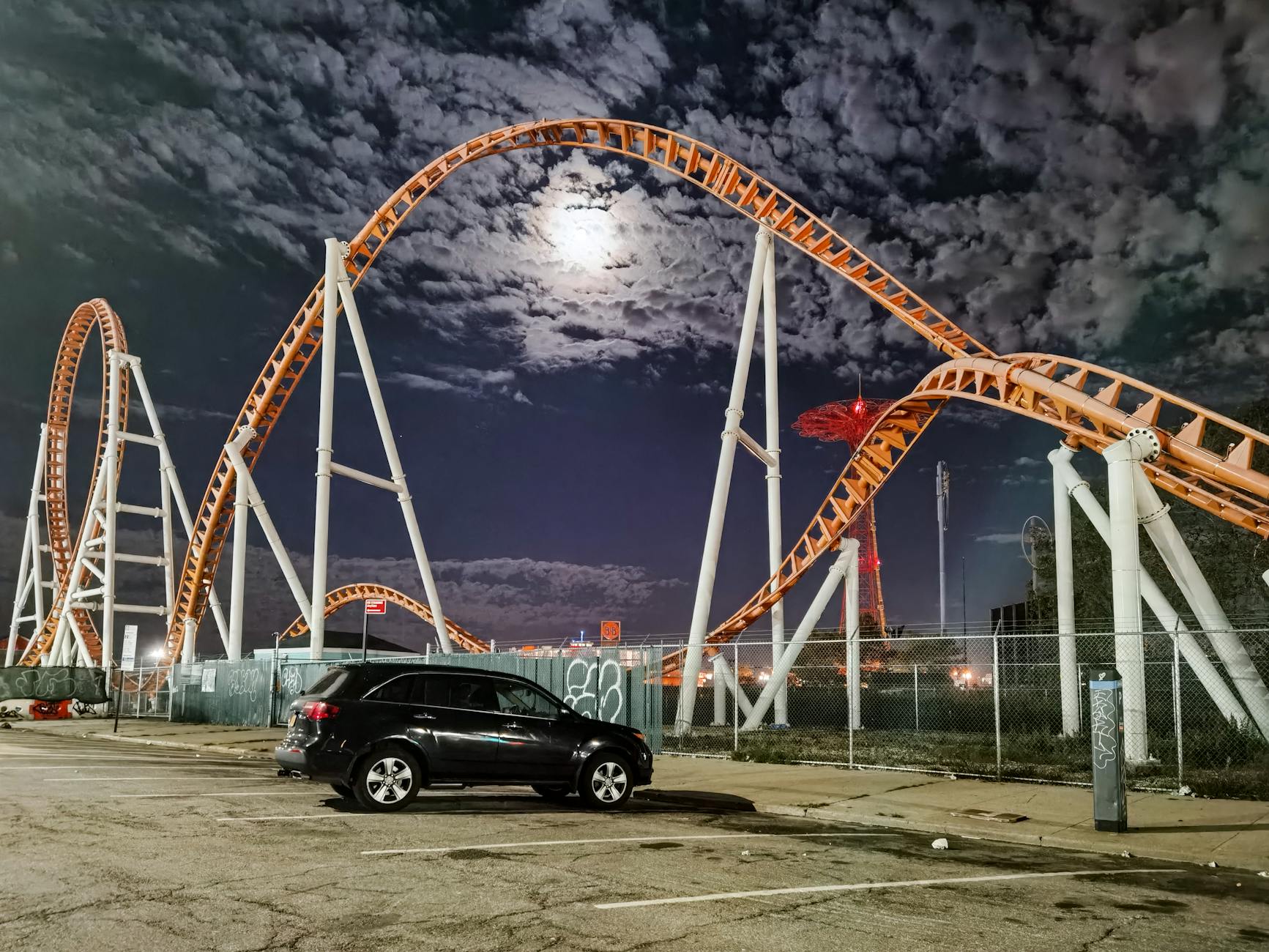 Nocny rollercoaster na tle księżyca i zaparkowanego samochodu