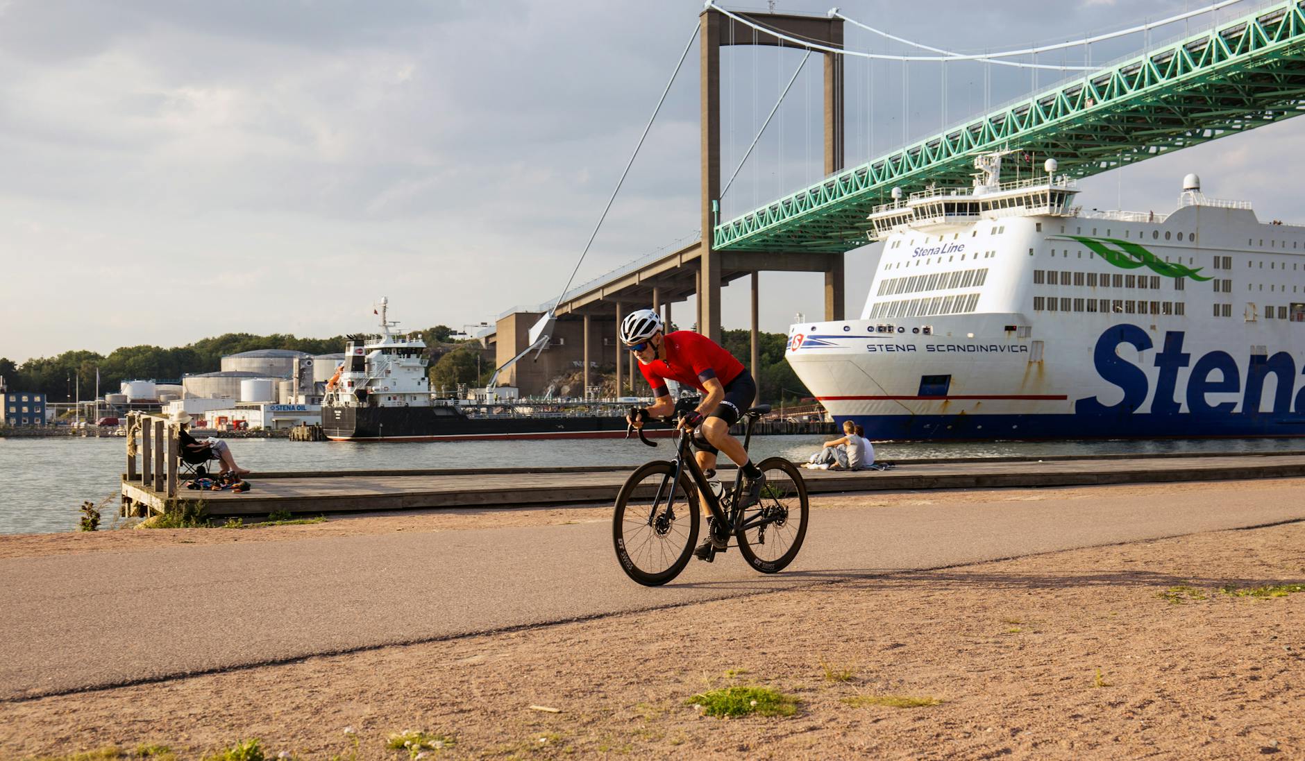 Mężczyzna na rowerze nad rzeką w Göteborgu, w tle most i prom